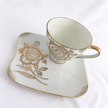 Load image into Gallery viewer, This vintage white porcelain teacup and saucer is absolutely stunning! The unique polygon shaped saucer and teacup are decorated with hand painted gold gilt roses and details. Produced in Japan. In good vintage condition, free from chips, cracks and repairs. Marked "Oakwood Hand Painted Japan". Teacup measures 3 3/14 x 2 3/4 inches | Saucer measures 5 3/4 x 5 x 5 3/4 inches