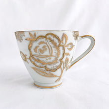 Load image into Gallery viewer, This vintage white porcelain teacup and saucer is absolutely stunning! The unique polygon shaped saucer and teacup are decorated with hand painted gold gilt roses and details. Produced in Japan. In good vintage condition, free from chips, cracks and repairs. Marked "Oakwood Hand Painted Japan". Teacup measures 3 3/14 x 2 3/4 inches | Saucer measures 5 3/4 x 5 x 5 3/4 inches