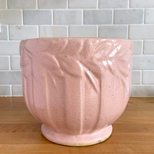 Load image into Gallery viewer, Rare vintage matte pink Sand Butterfly jardiniere planter with embossed vertical bands topped with a border of leaves and butterflies. Crafted by McCoy Pottery, 1930s. This rare planter is must for any McCoy art pottery collector. A wonderful piece to elevate your home and garden decor or to give as a gift!
In as found vintage condition, chips to the rim and crack, no repairs. Normal age-related crazing and manufacturer's glaze pops. Maker's mark on the bottom.
Measures 8 x 7 inches