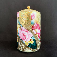 Load image into Gallery viewer, Absolutely exquisite vintage hand painted porcelain lidded ginger jar, crafted by artisans in Japan, late 1800s - early 1900s. It features sweeping panes of pink roses against a yellow and deep teal with alternating peacock feather-like shapes of gold gilt, heavily embellished with moriage, as is the lid. According to Kovels, Nippon Porcelain dates between 1891-1921. After that, US law required imports to be labeled with the country of origin in English. This one-of-a-kind piece.