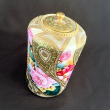 Load image into Gallery viewer, Absolutely exquisite vintage hand painted porcelain lidded ginger jar, crafted by artisans in Japan, late 1800s - early 1900s. It features sweeping panes of pink roses against a yellow and deep teal with alternating peacock feather-like shapes of gold gilt, heavily embellished with moriage, as is the lid. According to Kovels, Nippon Porcelain dates between 1891-1921. After that, US law required imports to be labeled with the country of origin in English. This one-of-a-kind piece.