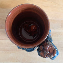 Load image into Gallery viewer, Rare vintage handmade Poseidon and Mermaid redware pottery mug finished in high fired two tone blue glaze on the exterior and a clear glazed interior. This large mug features a figural god of the sea wrapped around the exterior and mermaid in the interior of the mug. Crafted by KD Gandas, Lithuania 1990s. The perfect vessel for your favourite hot beverage!
In excellent condition with original sticker and impressed maker's mark.
Measures 6 1/4 x 4 1/4 x 6 1/2 inches (incl. handle)
Capacity 16 ounces