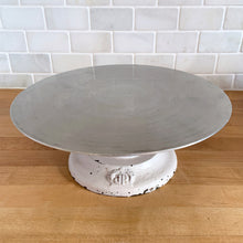 Load image into Gallery viewer, Vintage revolving cake decorating stand featuring a solid cast iron base and aluminum turntable. The base is painted in a putty colour and embossed with the initials JR inside a crown. Crafted by J. R. Mahoney for Crown Cookware, USA, 1930s. Perfect to use as intended, or to display cakes, baked good or use to create a special display of your favourite vintage treasures. A wonderful accessory for a vintage kitchen with a vintage or farmhouse theme or old fashioned bakery.
Vintage condition 12 x 4 1/2 inch