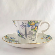 Load image into Gallery viewer, Vintage art deco white bone china teacup and saucer is absolutely gorgeous! Produced by Royal Albert, England, circa 1927 - 1935. Decorated in the "Rosalie" pattern which depicts a hand painted garden path featuring a trellis filled with blue, purple and yellow flowers, trimmed with gold gilt. Excellent condition, free from chips, cracks and repairs. Maker's marks are on the bottom. Teacup measures 3 3/8 x 2 3/4 inches | Saucer measures 5 1/4 inches