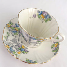 Load image into Gallery viewer, Vintage art deco white bone china teacup and saucer is absolutely gorgeous! Produced by Royal Albert, England, circa 1927 - 1935. Decorated in the "Rosalie" pattern which depicts a hand painted garden path featuring a trellis filled with blue, purple and yellow flowers, trimmed with gold gilt. Excellent condition, free from chips, cracks and repairs. Maker's marks are on the bottom. Teacup measures 3 3/8 x 2 3/4 inches | Saucer measures 5 1/4 inches