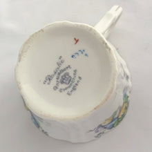 Load image into Gallery viewer, Vintage art deco white bone china teacup and saucer is absolutely gorgeous! Produced by Royal Albert, England, circa 1927 - 1935. Decorated in the "Rosalie" pattern which depicts a hand painted garden path featuring a trellis filled with blue, purple and yellow flowers, trimmed with gold gilt. Excellent condition, free from chips, cracks and repairs. Maker's marks are on the bottom. Teacup measures 3 3/8 x 2 3/4 inches | Saucer measures 5 1/4 inches
