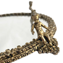 Load image into Gallery viewer, Stunning example of a vintage Hollywood Regency style round mirrored vanity tray featuring a border of brass filigree flower blossoms with a seated cherub on each of the four feet to guard your treasures. Adds a touch of glamour to bath or bedroom decor! In excellent used vintage condition. Measures 8 3/4 inches from foot to foot