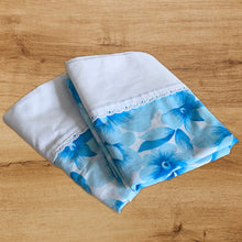 Load image into Gallery viewer, Vintage Serenity double/full poly cotton flat, fitted bed sheets, with two pillowcases. These linens feature a large scale blue floral print on white ground, finished with a white band and eyelet detail. Crafted by Wabasso, Canada, 1976 – 1979. Create a restful slumber with these beautifully designed and well-made linens, or repurpose for crafting, quilting or dressmaking!