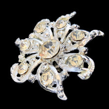 Load image into Gallery viewer, Angled front view of vintage silver-tone pinwheel brooch showing faceted clear rhinestones set in scrolling milgrain-edged openwork frame