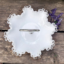 Load image into Gallery viewer, This vintage milk glass "Silver Crest" bon bon dish brings all the drama in a small package! It features a clear crimped edge over milk glass and a silver-toned metal handle. Crafted by the Fenton Art Glass, USA, circa 1960s. A graceful piece of pressed glass in a classic pattern that will always be in style no matter your decor style! Fill with your favourite candies, nuts or snacks. In excellent condition, free form chips/cracks. Measures 8 x 5 inches (incl. handle)