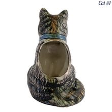 Load image into Gallery viewer, Vintage skillfully hand painted figural tabby cat ceramic planters with intense expressions. These planters have a distinct painting style and date to the 1930s. Features a dark charcoal tabby cat with soulful gray eyes and gray ears, wearing a blue bow tie. In excellent condition, free from chips/cracks/repairs. Impressed mark on the bottom reads, Made in Japan. Measure 6 1/8 x 4 1/2 x 7 inches