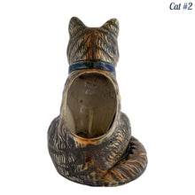 Load image into Gallery viewer, Vintage skillfully hand painted figural tabby cat ceramic planters with intense expressions. These planters have a distinct painting style and date to the 1930s. Features dark charcoal and brown tabby cat with piercing green eyes, pink ears, wearing a blue bow tie. In excellent condition, free from chips/cracks/repairs. Impressed mark on the bottom reads, Made in Japan. Measure 6 1/8 x 4 1/2 x 7 inches