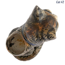 Load image into Gallery viewer, Vintage skillfully hand painted figural tabby cat ceramic planters with intense expressions. These planters have a distinct painting style and date to the 1930s. Features dark charcoal and brown tabby cat with piercing green eyes, pink ears, wearing a blue bow tie. In excellent condition, free from chips/cracks/repairs. Impressed mark on the bottom reads, Made in Japan. Measure 6 1/8 x 4 1/2 x 7 inches