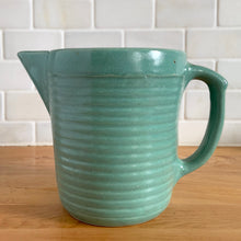Load image into Gallery viewer, Vintage teal glazed horizontal ribbed stoneware pitcher. Crafted by Monmouth Western Stoneware, USA, 1920s. Add this solid utilitarian piece to your farmhouse decor or art pottery collection!
In excellent condition, no chips/cracks/repairs, age-related crazing. Maker's mark.
Measures 7 3/8 x 4 1/2 x 5 inches (incl. spout and handle)