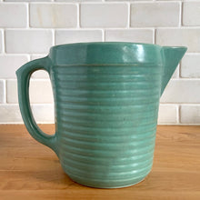 Load image into Gallery viewer, Vintage teal glazed horizontal ribbed stoneware pitcher. Crafted by Monmouth Western Stoneware, USA, 1920s. Add this solid utilitarian piece to your farmhouse decor or art pottery collection!
In excellent condition, no chips/cracks/repairs, age-related crazing. Maker's mark.
Measures 7 3/8 x 4 1/2 x 5 inches (incl. spout and handle)