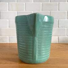 Load image into Gallery viewer, Vintage teal glazed horizontal ribbed stoneware pitcher. Crafted by Monmouth Western Stoneware, USA, 1920s. Add this solid utilitarian piece to your farmhouse decor or art pottery collection!
In excellent condition, no chips/cracks/repairs, age-related crazing. Maker's mark.
Measures 7 3/8 x 4 1/2 x 5 inches (incl. spout and handle)