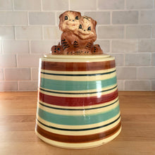 Load image into Gallery viewer, Adorable vintage hand painted ceramic cookie jar topped with a pair of anthropomorphic tiger cubs on a barrel with horizontal stripes in brown, black, turquoise and cranberry on a beige ground. Robinson Ransbottom Pottery Co., 1950s. A excellent example of mid-century era kitsch. Add this darling cookie jar to your kitchen decor or cookie jar collection!
In overall great condition with worn chips on the ears and age-related crazing. Marked R.R.P. Co. Roseville Ohio No - 386.
Measures 7 1/4 x 10 inches