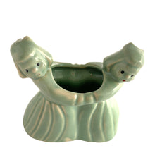 Load image into Gallery viewer, Sweet vintage ceramic planter featuring two dancing Dutch girls, finished in pale green glaze. Crafted by McCoy Pottery, USA, circa 1930s. Perfect to use a decor piece, a tiny houseplant or repurpose to hold make-up brushes. Makes an excellent gift! In excellent condition, free from chips/cracks. Measures 4 3/4 x 2 3/8 x 4 1/2 inches