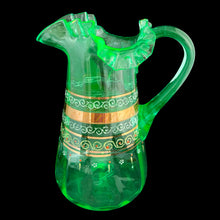 Load image into Gallery viewer, Antique Victorian era green uranium glass pitcher featuring gold, white and red enamel decoration with ruffle crimped rim and an applied handle. Glows beautifully under black light. Crafted by Fenton Art Glass, USA, early 20th century. A stunning piece to add to your glass collection.
In as found vintage condition with wear to the enamel. There is a stringer in the handle and a chip to the base of the handle itself.
Measures 5 3/4 x 8 x 10 inches