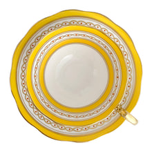 Load image into Gallery viewer, This antique bone china footed teacup and saucer is so sweet! Both the cup and saucer have a lovely scalloped edge, hand painted gold gilt bands over yellow and white glazed porcelain and a gold gilt infinity ribbon dotted in orange. Produced by Royal Albert Crown China, England. Based on the maker's mark, dates to 1927 - 1935. In excellent condition, free from chips, cracks or repairs. Maker's mark on the bottom of both pieces. Teacup is marked with the number 591.
