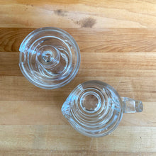 Load image into Gallery viewer, Rare vintage modernist clear glass stackable creamer and covered sugar. Designed by Joe Colombo for Arno, Italy, 1960s. Each piece has a sleek geometric design with a silhouette that makes the contents in this pressed glass appear suspended above the table surface.
Both the creamer and sugar are in excellent condition, no chips or cracks and minimal wear.
Sugar bowl measures 3 3/8 x 3 3/8 x 3 3/8 inches
Creamer measures 4 x 3 3/8 x 3 1/4 inches