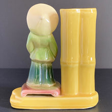 Load image into Gallery viewer, A vintage ceramic vase of planter in the Chinoiserie style features a green and red Asian figure with a yellow bamboo vase on a podium, shape 702. Crafted by Shawnee Pottery USA. Perfect as a bud vase or to a decor accent.
In good vintage condition, no cracks. Small glaze miss on the front of the podium.
Measures 5 x 2 1/2 x 5 1/2 inches
