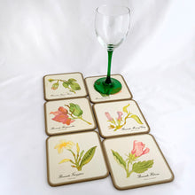 Load image into Gallery viewer, A vintage set of six square round edged coasters, each decorated with an illustration of a tropical flower on an off-white background, bordered in gold with cork-backing. Coasters make the perfect resting place for drinking glasses or mugs to protect your furniture from being marked. Made by Pimpernel in England. Makes a great housewarming or hostess gift! In excellent vintage condition. Each coaster measures 4-1/8" x 4-1/8"