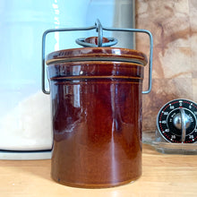 Load image into Gallery viewer, Vintage dark brown glazed pottery storage crock with wire bail closure. Maker unknown. Made in the USA and marked 1059¢ on the bottom. Take the lid off and repurpose as a pencil/pen/make-up brush holder, planter change holder, or use as a decor piece. In excellent condition, free from chips/cracks/repairs. Measures 3-1/4" x 5"