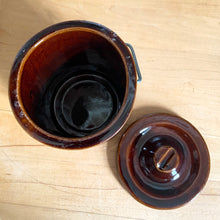 Load image into Gallery viewer, Vintage dark brown glazed pottery storage crock with wire bail closure. Maker unknown. Made in the USA and marked 1059¢ on the bottom. Take the lid off and repurpose as a pencil/pen/make-up brush holder, planter change holder, or use as a decor piece. In excellent condition, free from chips/cracks/repairs. Measures 3-1/4" x 5"