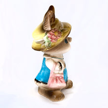Load image into Gallery viewer, Adorable vintage figural brown bunny rabbit coin bank dressed in blue with a pink purse and yellow hat. Unmarked but likely made in Japan or Taiwan, circa 1970s. In great vintage condition with a flea bite to one of the feet. Measures approximately 6" tall.