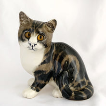 Load image into Gallery viewer, Highly desirable and collectible, this sweet vintage ceramic seated grey/brown striped tabby cat figurine has striking amber cathedral glass eyes (if you look at the eyes and move, the eyes will follow you). Produced by artist Mike Hinton, England (retired from Winstanley). In excellent condition, free from chips/cracks. Signed by the artist and marked with the # 33 and England. Dimensions: 5-1/4" x 3-3/4" x 5-3/4"
