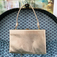 Load image into Gallery viewer, Stunning mid-century vintage gold lamé evening bag with gold toned oval button flip clasp, top strap handle and the interior is lined with gold satin. The bag is large enough for a cell phone, credit cards/cash, small compact/lipstick. Crafted by After Five, USA, 1950s. Adds a dash of Hollywood glam to your fashion statement!
In vintage condition with age-related wear. Maker's mark on the interior.
Measures 7 3/4 x 1 x 5 inches, 5 1/8 inch handle drop