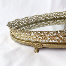 Load image into Gallery viewer, This elegant vintage Hollywood Regency style oval-shaped mirrored dresser vanity tray, featuring brass ormolu details, is perfect for displaying perfume bottles, trinket dishes, and makeup. Alternately, hang it on the wall to add glitz and glamour to your décor. In excellent condition. Measures 12 x 9 x 1 1/4 inches
