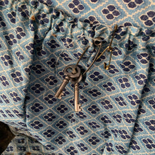 Load image into Gallery viewer, black vintage round train case or suitcase with nice blue and white floral/diamond patterned lining, a leather handle, brass latches and locking mechanism with TWO original keys. Exterior has two stickers, HAPAG shipping company and a customs inspection sticker. Well worn leather handle. All hardware is in good working order and the case opens and closes nicely. The case has normal wear from 80 plus years of usage, but no major damage. measures 16-1/2" tall and 18" wide, and 9" deep.
