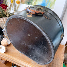 Load image into Gallery viewer, black vintage round train case or suitcase with nice blue and white floral/diamond patterned lining, a leather handle, brass latches and locking mechanism with TWO original keys. Exterior has two stickers, HAPAG shipping company and a customs inspection sticker. Well worn leather handle. All hardware is in good working order and the case opens and closes nicely. The case has normal wear from 80 plus years of usage, but no major damage. measures 16-1/2" tall and 18" wide, and 9" deep.