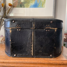 Load image into Gallery viewer, black vintage round train case or suitcase with nice blue and white floral/diamond patterned lining, a leather handle, brass latches and locking mechanism with TWO original keys. Exterior has two stickers, HAPAG shipping company and a customs inspection sticker. Well worn leather handle. All hardware is in good working order and the case opens and closes nicely. The case has normal wear from 80 plus years of usage, but no major damage. measures 16-1/2" tall and 18" wide, and 9" deep.
