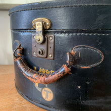 Load image into Gallery viewer, black vintage round train case or suitcase with nice blue and white floral/diamond patterned lining, a leather handle, brass latches and locking mechanism with TWO original keys. Exterior has two stickers, HAPAG shipping company and a customs inspection sticker. Well worn leather handle. All hardware is in good working order and the case opens and closes nicely. The case has normal wear from 80 plus years of usage, but no major damage. measures 16-1/2" tall and 18" wide, and 9" deep.