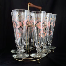 Load image into Gallery viewer, Make any day a special occasion with these highly collectible and hard to find vintage mid-century atomic style Seville pilsner or champagne glasses. Decorated with a graphic geometric design in swirls of pink, charcoal black and gold, they remind us of a New Year's eve party and are perfect for that midnight champagne toast! Bonus, they come in the original wood handled brass caddy.