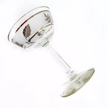 Load image into Gallery viewer, Vintage mid-century Silver Leaf champagne coupe or martini glass featuring silver leaves set on a frosted band, silver bands, grecian column stem. Crafted by Libbey Glass, USA, 1953 - 1978. These put the "glam" in glamourous — a stunning addition to your barware collection and perfect for ringing in the New Year with a toast! Also makes a wonderful wedding or housewarming gift for any cocktail enthusiast.
In excellent condition, no chips. Minimal wear.
Measures 3 3/4 x 5 5/8 inches
Capacity 7 ounces