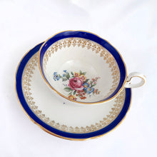 Load image into Gallery viewer, This vintage bone china teacup and saucer is absolutely stunning! Both the cup and saucer are glazed in white with a blue band, gold geometric pattern and rim with a central bouquet of colourful flowers. Produced by Royal Grafton, England, circa 1950 - 1956. In excellent condition, free from chips, cracks and repairs. Pattern number 1781 marked on the bottom of the teacup. Teacup measures 3-7/8" x 2" | Saucer measures 5-5/8"