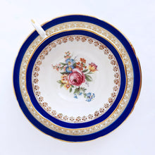 Load image into Gallery viewer, This vintage bone china teacup and saucer is absolutely stunning! Both the cup and saucer are glazed in white with a blue band, gold geometric pattern and rim with a central bouquet of colourful flowers. Produced by Royal Grafton, England, circa 1950 - 1956. In excellent condition, free from chips, cracks and repairs. Pattern number 1781 marked on the bottom of the teacup. Teacup measures 3-7/8" x 2" | Saucer measures 5-5/8"