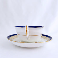 Load image into Gallery viewer, This vintage bone china teacup and saucer is absolutely stunning! Both the cup and saucer are glazed in white with a blue band, gold geometric pattern and rim with a central bouquet of colourful flowers. Produced by Royal Grafton, England, circa 1950 - 1956. In excellent condition, free from chips, cracks and repairs. Pattern number 1781 marked on the bottom of the teacup. Teacup measures 3-7/8" x 2" | Saucer measures 5-5/8"