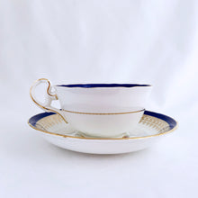 Load image into Gallery viewer, This vintage bone china teacup and saucer is absolutely stunning! Both the cup and saucer are glazed in white with a blue band, gold geometric pattern and rim with a central bouquet of colourful flowers. Produced by Royal Grafton, England, circa 1950 - 1956. In excellent condition, free from chips, cracks and repairs. Pattern number 1781 marked on the bottom of the teacup. Teacup measures 3-7/8" x 2" | Saucer measures 5-5/8"