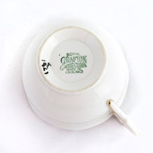 Load image into Gallery viewer, This vintage bone china teacup and saucer is absolutely stunning! Both the cup and saucer are glazed in white with a blue band, gold geometric pattern and rim with a central bouquet of colourful flowers. Produced by Royal Grafton, England, circa 1950 - 1956. In excellent condition, free from chips, cracks and repairs. Pattern number 1781 marked on the bottom of the teacup. Teacup measures 3-7/8" x 2" | Saucer measures 5-5/8"