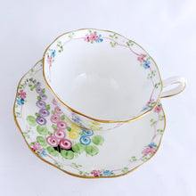 Load image into Gallery viewer, This antique bone china footed teacup and saucer is so sweet! Both the cup and saucer have a lovely scalloped edge with hand painted whimsical pastel coloured foxglove flowers and rimmed with gold gilt. Produced by Royal Albert, England, circa 1917 - 1927. In good condition. Teacup measures 3 3/4 x 2 3/8 inches | Saucer measures 5 1/2 inches