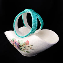 Load image into Gallery viewer, This vintage mid-century hand crafted folded white ceramic pottery basket, features a matte white glaze hand painted with colourful flowers and topped with a uniquely shaped turquoise folded infinity handle. The pottery has a slight texture which adds to its charm. Made in Italy. It's just that gorgeous! In excellent condition, free from chips/cracks/repairs. Marked on the bottom with "671/159 Italy" Measures 8 7/8 x 4 3/4 x 6 1/2 inches