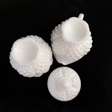 Load image into Gallery viewer, Vintage white milk glass is the epitome of simple elegance! This is a scalloped creamer and lidded sugar bowl in the "Hobnail" pattern. Produced by Fenton, post 1970. Marked. The creamer is in excellent condition, free from chips or cracks. The sugar bowl has a chip on the side of one of the scalloped points...it's not rough or really noticeable thanks to the piece being white. Creamer measures 4" 3-1/2", sugar w/ lid measures 4" x 4-3/4"
