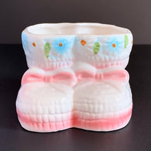 Load image into Gallery viewer, Vintage white baby booties ceramic planter features pink bows, white and blue flowers. Crafted by Nancy Pew Giftware, Taiwan, 1970s. An adorable accessory for a baby nursery!
In excellent condition, no chips, cracks or repairs. Maker's mark and sticker.
Measures 4 x 4 x 3 inches