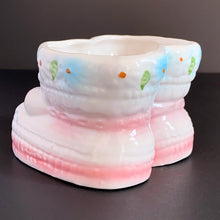 Load image into Gallery viewer, Vintage white baby booties ceramic planter features pink bows, white and blue flowers. Crafted by Nancy Pew Giftware, Taiwan, 1970s. An adorable accessory for a baby nursery!
In excellent condition, no chips, cracks or repairs. Maker's mark and sticker.
Measures 4 x 4 x 3 inches