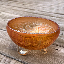 Load image into Gallery viewer, This vintage Two Flowers marigold carnival glass bowl features an intricate design of dogwood flowers and marsh lilies, a smooth sawtooth rim and three spatulate feet. Crafted by Fenton Art Glass, early 20th century. The iridescence on this bowl is outstanding and it's sure to become a treasured heirloom. In excellent condition, no chips. Measures 6 1/4 x 3 1/2 inches